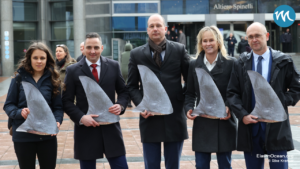 Dekoratives Bild: Vor dem EU-Parlament in Brüssel. Fünf Personen halten Haifisch-Rückenflossen in die Kamera und schauen ernst.
